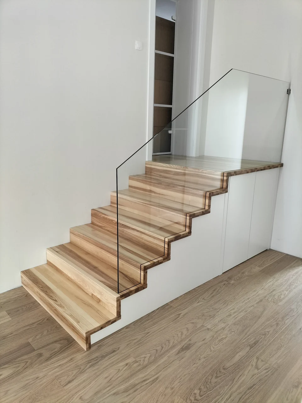 Schody dywanowe ze szklaną balustradą i zabudową pod schodami